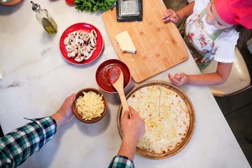 Overhead view of father and daughter preparing homemade pizza in the kitchen.